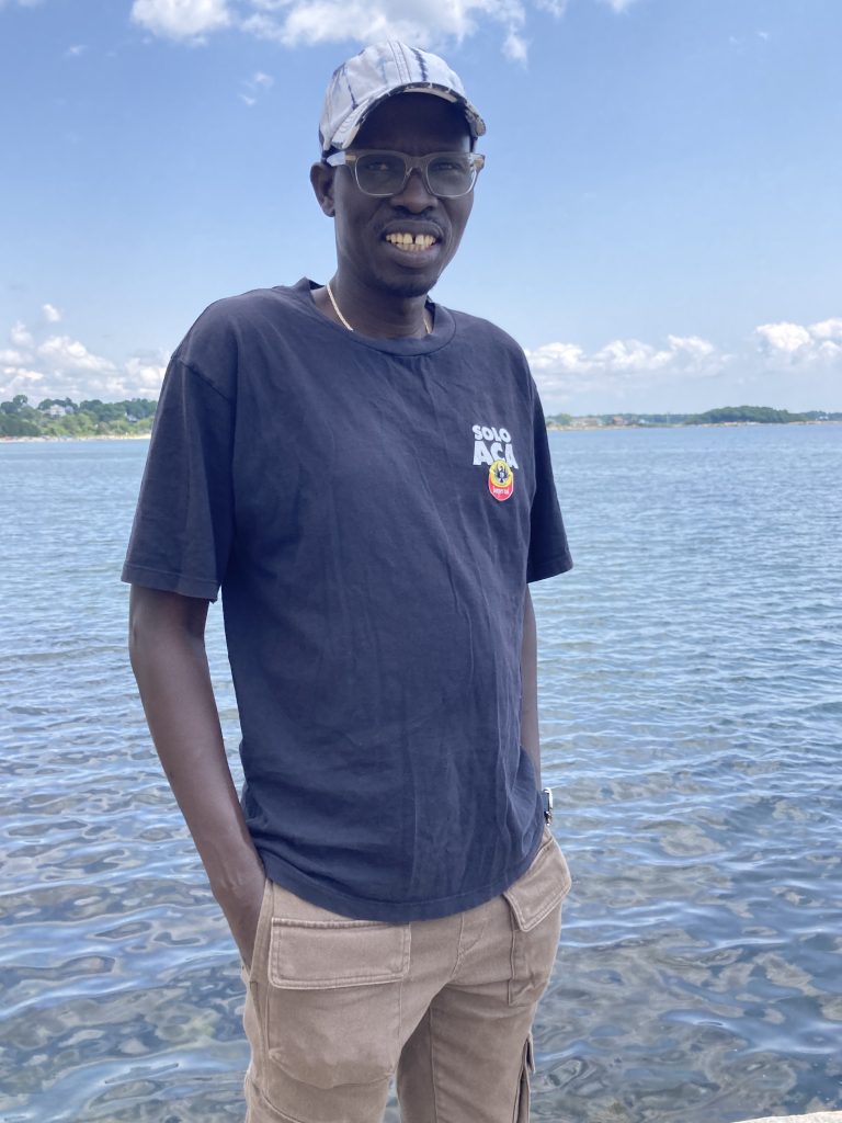 Former student Kwot Jay smiling in front of a body of water