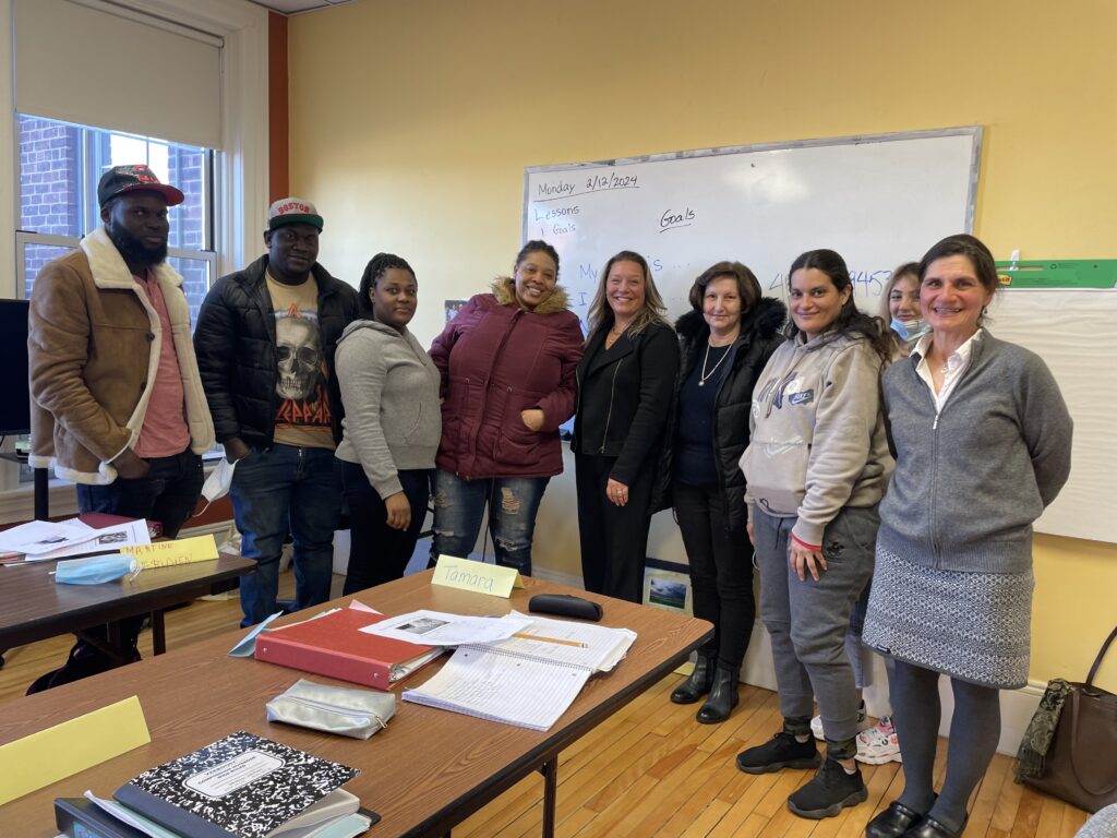 A group of adult ESOL education students with state representative Natalie M Blais in front of a whiteboard in a CNA classroom