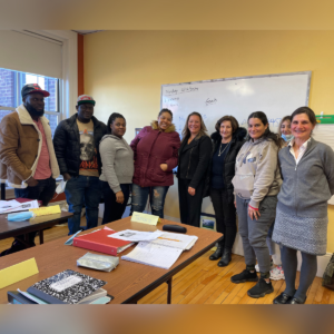 A group of adult ESOL education students in teacher Tamara's class with state representative Natalie M Blais in front of a whiteboard in a CNA classroom