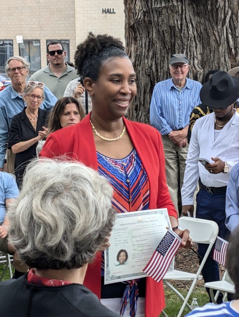 A smiling woman holding her naturalization certificate and an American flag
